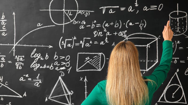 blonde woman pointing to a scientific equation on the black board